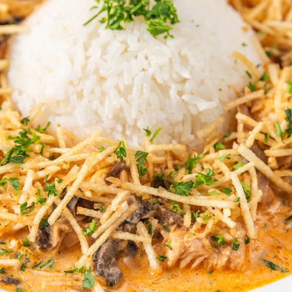 Creamy salmon and mushroom stroganoff with crispy potato sticks and a mound of white rice.