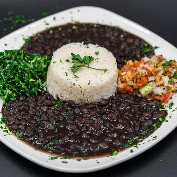 A white plate with black beans, white rice, green collard greens, and pico de gallo.