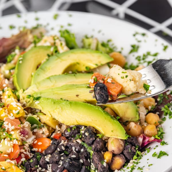 Colorful vegan salad with avocado, black beans, chickpeas, and salsa, with a fork lifting some food.