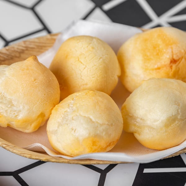 Golden-brown Brazilian cheese bread (pão de queijo) served in a woven basket on a patterned tablecloth.