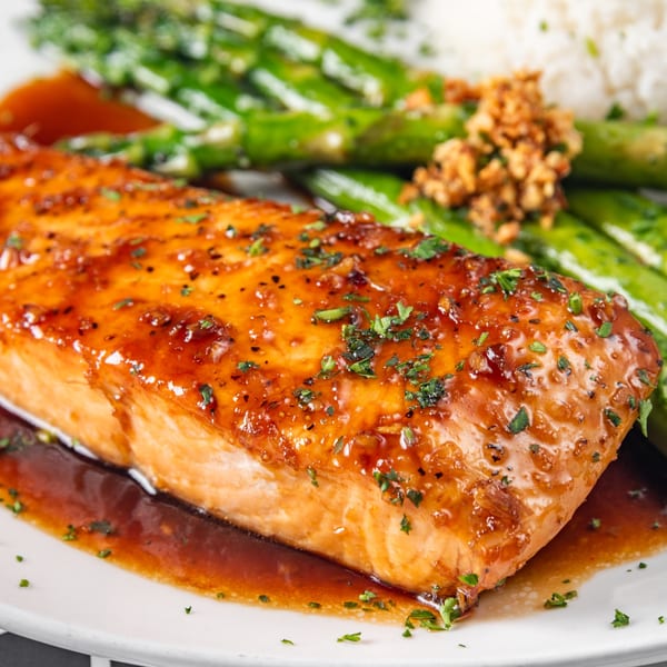 Glazed salmon with asparagus, white rice, and crispy garlic on a white plate.