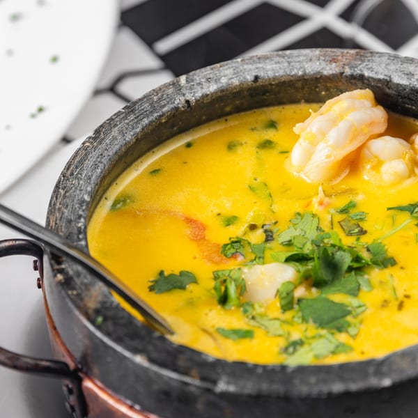 Bright yellow shrimp moqueca, garnished with fresh cilantro, served in a rustic stone pot.
