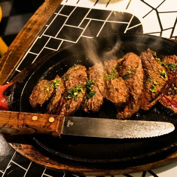 Sizzling steak slices with herbs on a hot plate, accompanied by a steak knife.