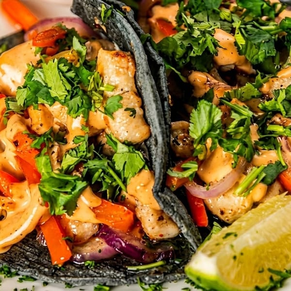 Two chicken tacos with black tortillas, red peppers, onions, cilantro, and a creamy sauce.